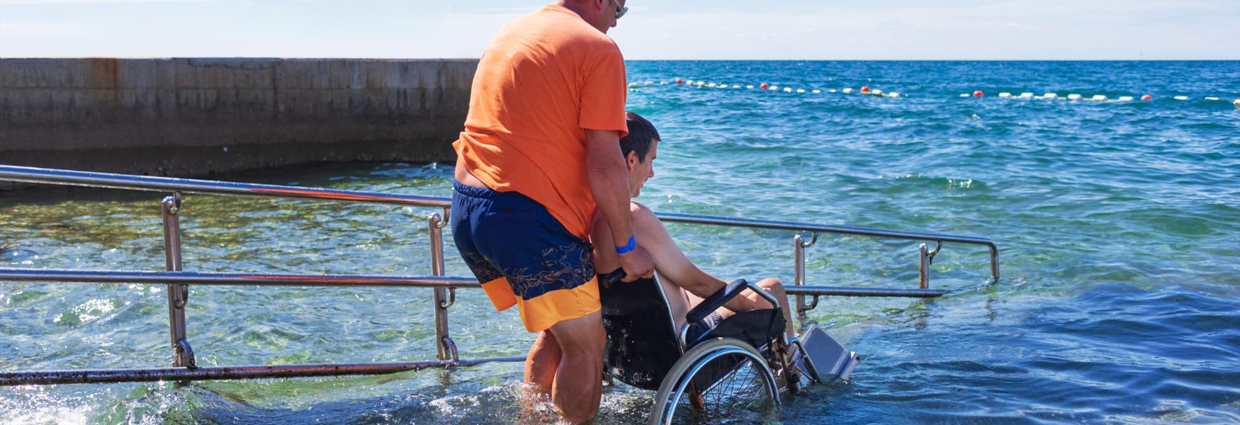 MAN PUSHING WHEELCHAIR USES DOWN A RAMP INTO  THE SEA