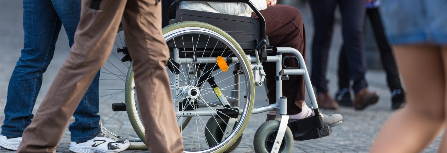 Close up image of person sat in wheelchair and the wheels and people walking