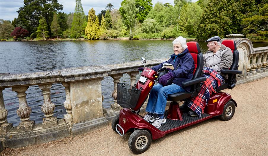 Two people riding an all terrain mobility scooter with two seats at Sheffield Park and Gardens