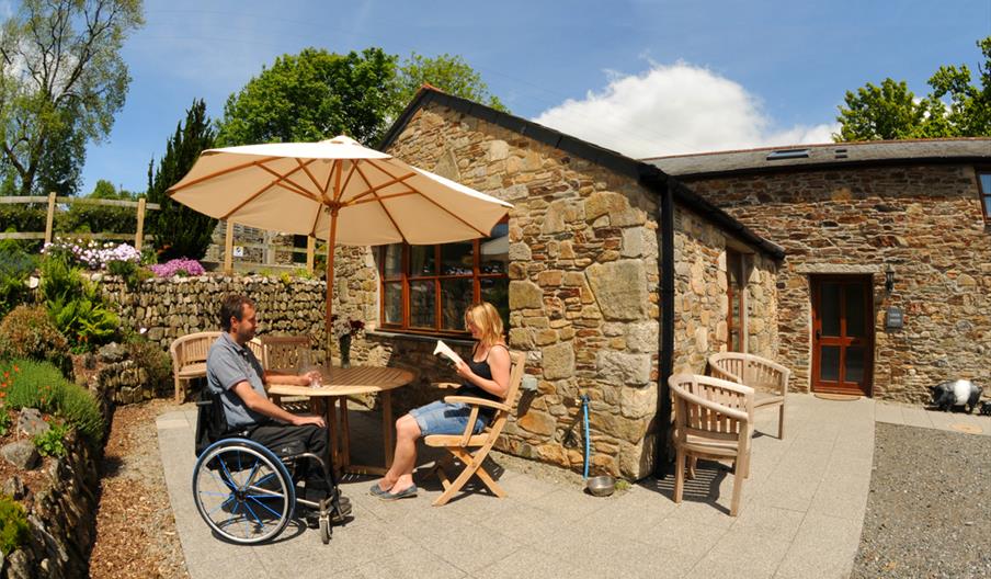 Guests sat outside cottage at Todsworthy Farm Holidays, one in a wheeldhair and another in a chair under a parasol