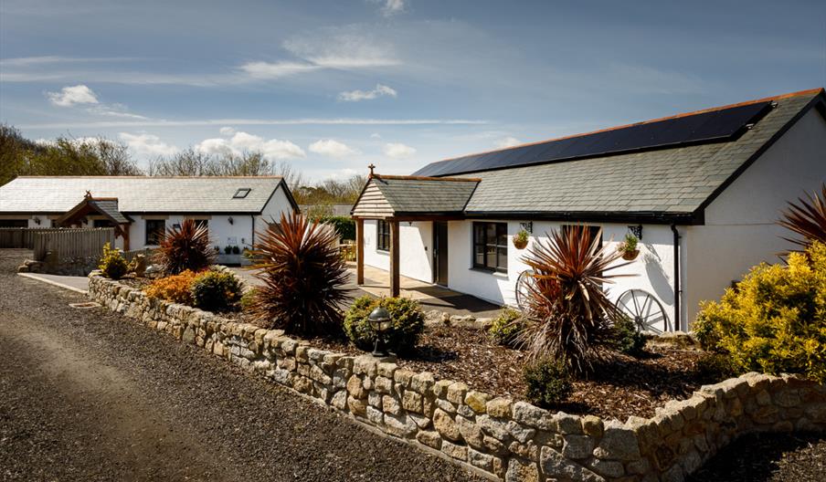 Outside of The Coach House Cornwall shows two white buildings with a garden that has some plants in it.
