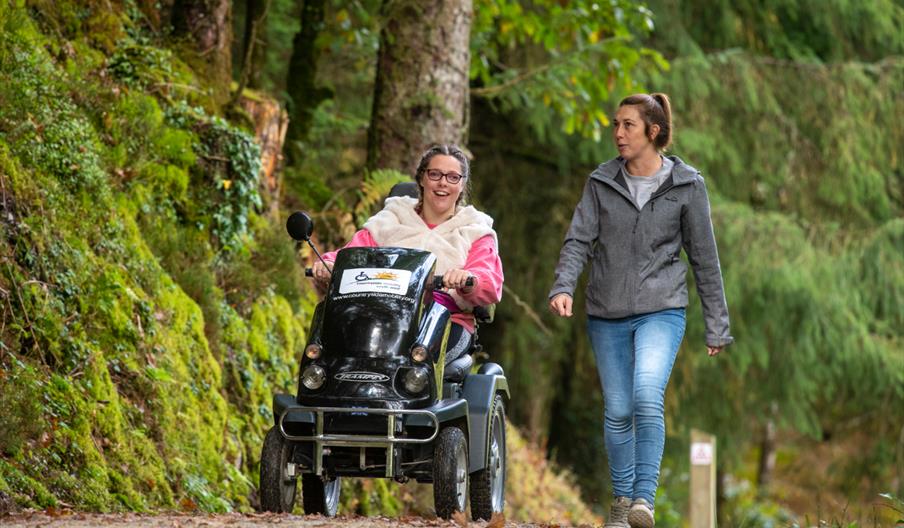 Two people exploring Cardinham Woods, one on foot and one in an all terrain wheelchair