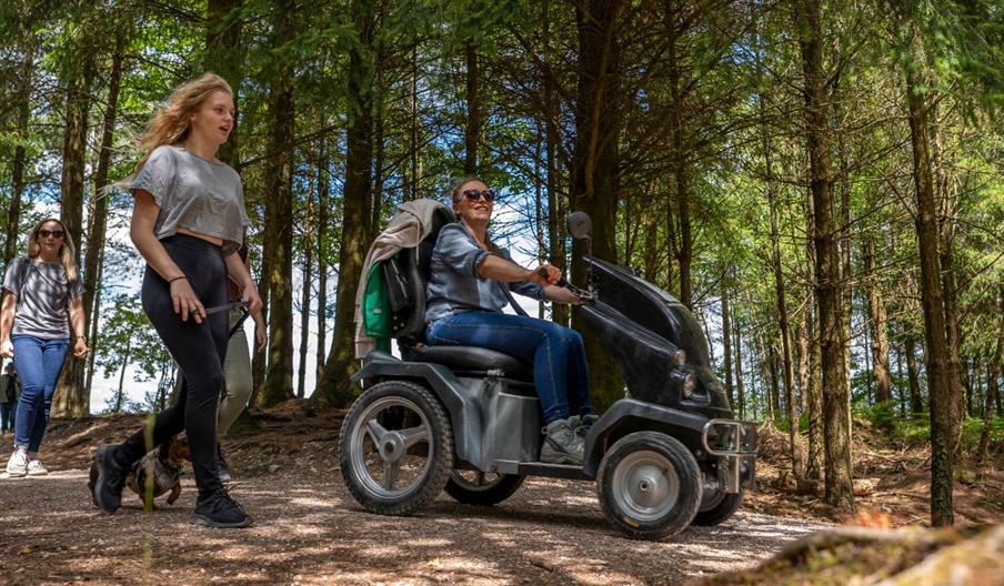 Group of women enjoying the trails at Haldon Forest Park with one person riding in an all terrain tramper