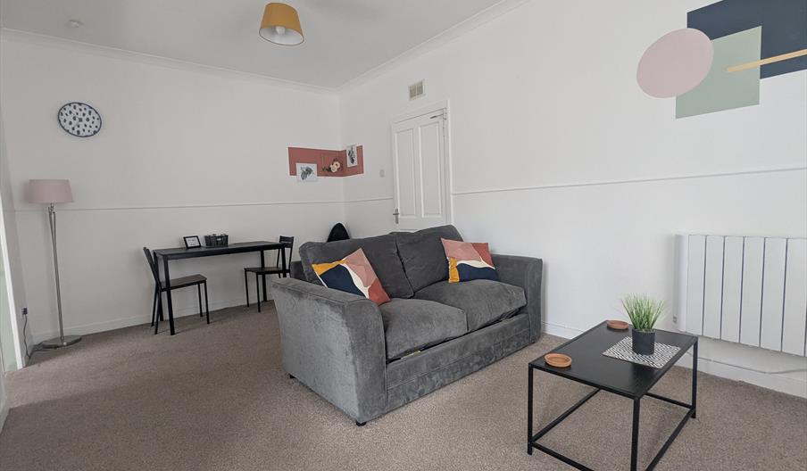 Grey sofa in the living room, which has some colourful cushions, with a coffee table infront