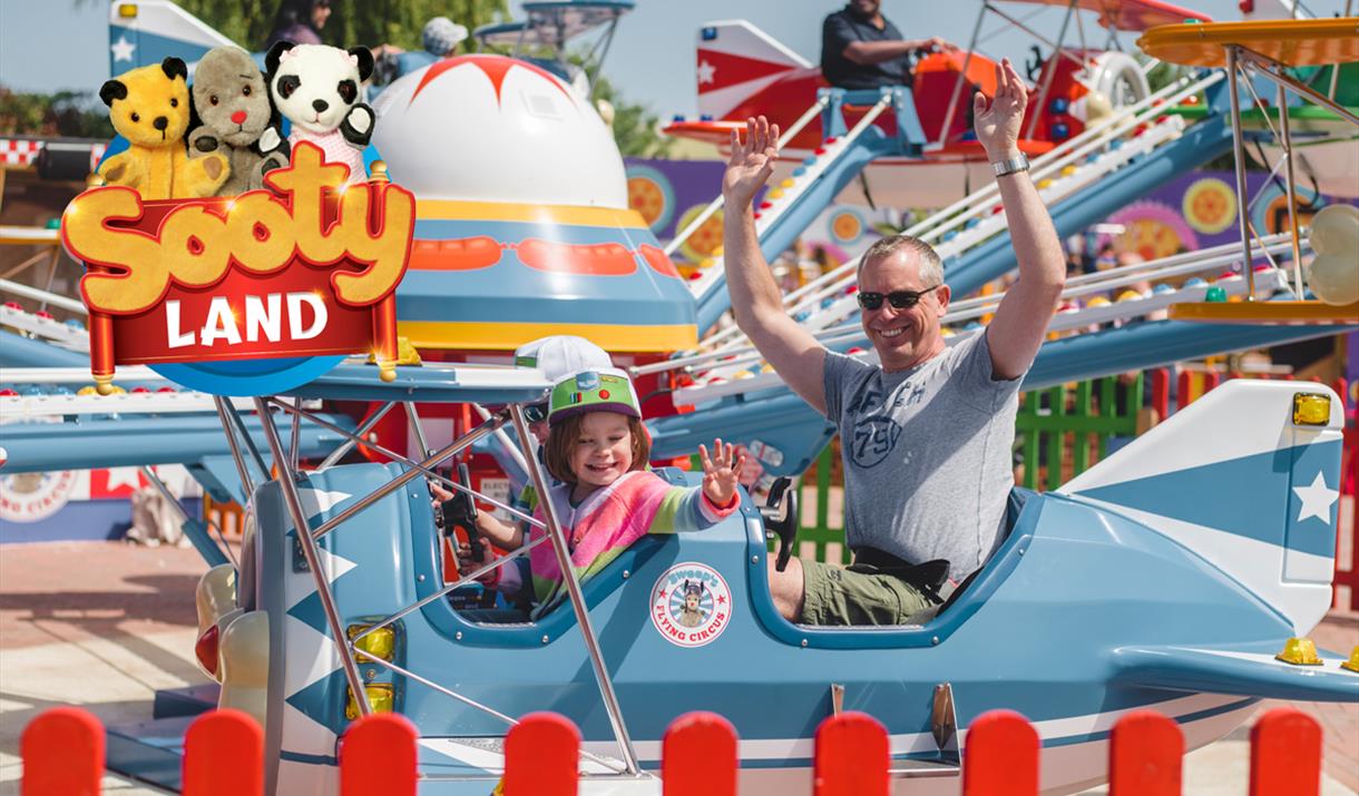 A parent and child on a plane ride at Crealy Theme Park with a Sooty Land logo over the top left corner