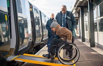 Person in a wheelchair boarding a GWR train via the ramp with station staff assisting