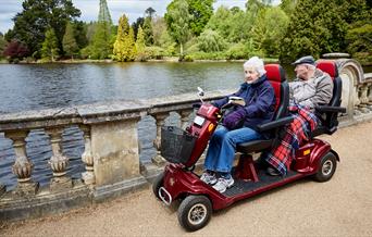 Two people riding an all terrain mobility scooter with two seats at Sheffield Park and Gardens