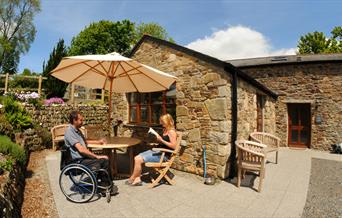 Guests sat outside cottage at Todsworthy Farm Holidays, one in a wheeldhair and another in a chair under a parasol