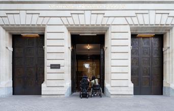 Two people in wheelchairs outside the main entrance of the National Portrait Gallery