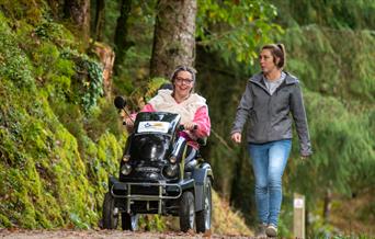 Two people exploring Cardinham Woods, one on foot and one in an all terrain wheelchair