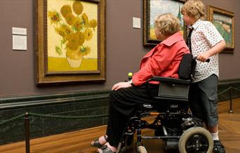 Person in a wheelchair with a companion looking at van gough's sunflowers at The National Gallery Trafalgar Square