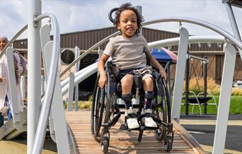 Child in a wheelchair on an accessible playground ramp.