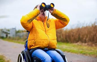 A child in a yellow coat and sat in a wheelchair with binoculars at WWT Arundel Wetland Centre