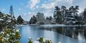 The lake frozen with snow in the surrounding trees at Sheffield Park and Gardens