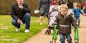 Little boy using a mobility aid to follow the path Sheffield Park and Gardens with other children and families in the background