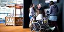 A family, featuring a girl in a wheelchair with a cast on her leg, and her parents and sibling looking at displays at Winchester Science Centre and Pl