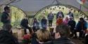 a group of people sat underneath a canopy listening to someone giving a presentation outdoors at explore!