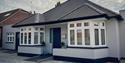 Entry to AbleStay, a grey bungalow style building with a wheelchair ramp leading up to the front door