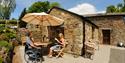 Guests sat outside cottage at Todsworthy Farm Holidays, one in a wheeldhair and another in a chair under a parasol