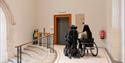 Two people in wheelchairs heading towards the lifts at National Portrait Gallery