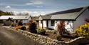 Outside of The Coach House Cornwall shows two white buildings with a garden that has some plants in it.