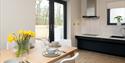 dining table, laid out with plates and bowls, with daffodils in a vase. In the background is the kitchen surfaces and doors leading outside