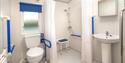 Accessible bathroom with hand rails and a shower chair at John Fowler Holiday Parks