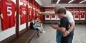 A boy being shown the football shirts in the locker room at LFC Stadium by his father