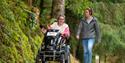 Two people exploring Cardinham Woods, one on foot and one in an all terrain wheelchair