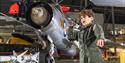 a boy in a green boiler suit standing in front of a plane at Imperial War Museum Duxford