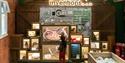 A young child stands in front of an exhibit titled "Amazing inventions..." in a museum or educational space. The display consists of various illuminat