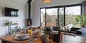 Oak Tree Cabin dining table with wood burner in the background. The bi-fold doors open to countryside views.
