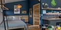 Double bed with grey sheets, surrounded by navy blue walls and wooden furnishing