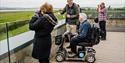 People birdwatching from one of the hides at WWT Slimbridge Wetland Centre, three people on foot looking through binoculars and one person in a wheelc