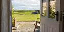 Looking through the door at Asheston Eco Barns onto the grounds with a paved area with a picnic table and green views
