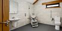 Coach House Cornwall accesisble bathroom with a toilet, some grab rails and a shower chair. The floor is level and wet room style.