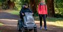 A couple following the paths at Bedgebury National Pinetum and Forest, one on foot and one in an all terrain wheelchair