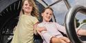 Two children on a ride in an amusement park, holding onto metal bars.