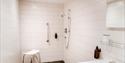 Wet room with hand rails and shower chair at Sandhole Cottages