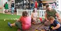 a mother is playing with her three children. Two girls and a boy on fake grass inside a play arena.