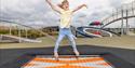 Child jumping on a trampoline at a playground with equipment in the background.