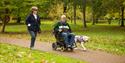 A couple following the paths at Petworth House & Park, one on foot and one in a wheelchair with a service dog