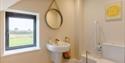 A light beige bathroom with an accessible toilet and lowered sink. A bright poster on the wall reads 'Rise and Shine'