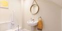An accessible bathroom with a lowered sink and a gold, circular mirror hanging on the wall.