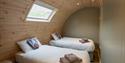 Cosy wood-paneled attic bedroom with two neatly made beds, skylight, folded towels, decorative pillows, and warm, peaceful lighting.