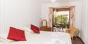 Hall Farm Cottage Bedroom showing a white bed with red cushions, a chair and open doorway to the courtyard