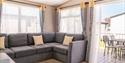 Living area with grey corner sofa and balcony with table and chairs in an accessible caravan at Beverley Holidays