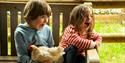 Two young children smiling and laughing while holding a chicken