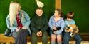 A mother and children with small animals. A boy has a white chicken on his head, a girl has a guinea pig on her lap and a young boy is holding a rabbi