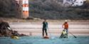 A group of people stand up paddleboarding, one supporting a disabled visitor with Healing Waves